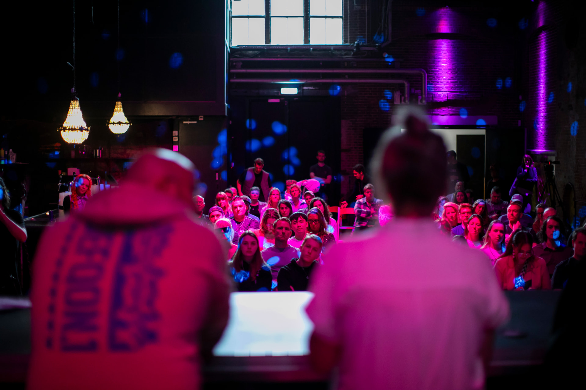 Panel speakers seen from behind facing a seated audience in warm light