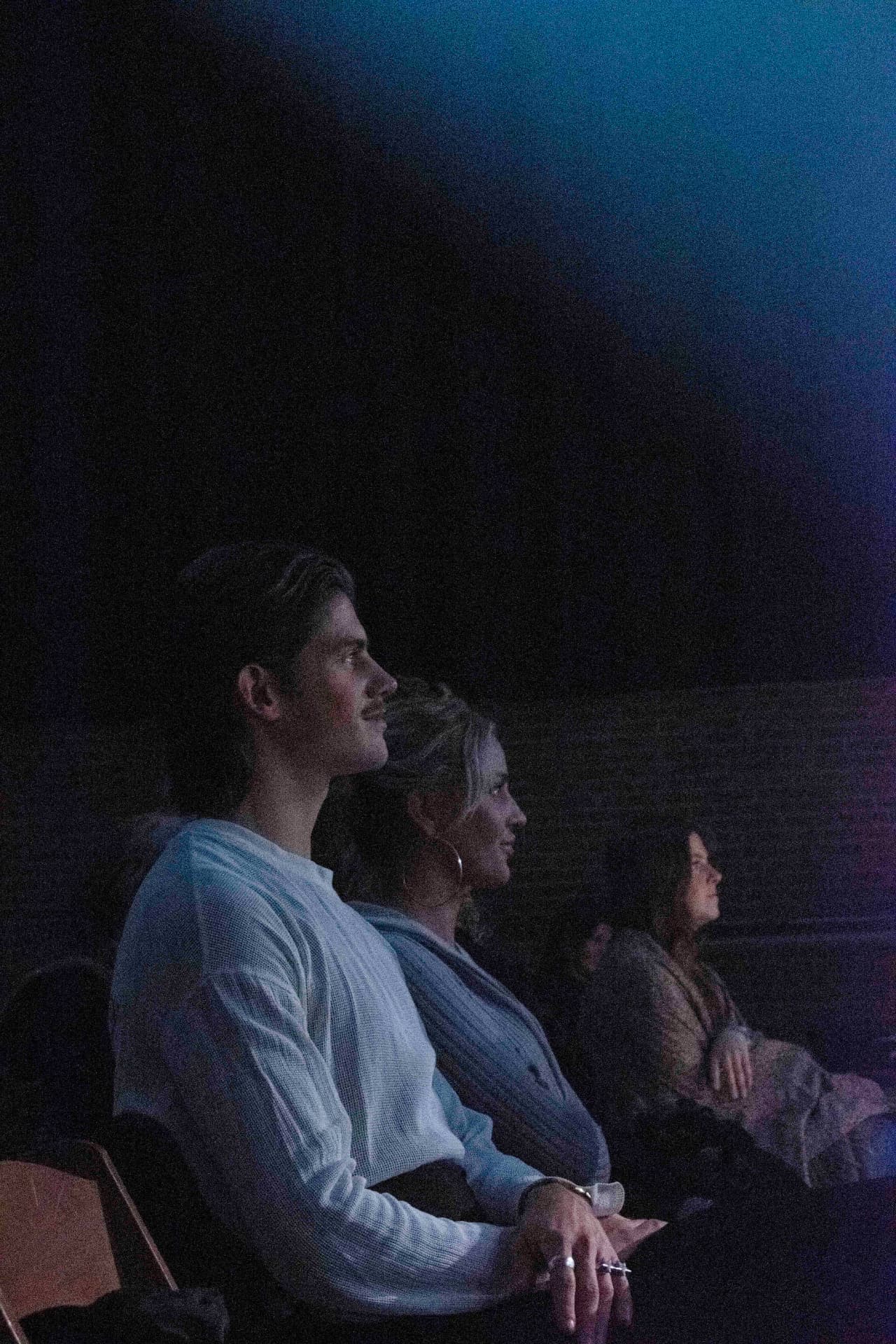 Seated audience members listening in deep blue stage light