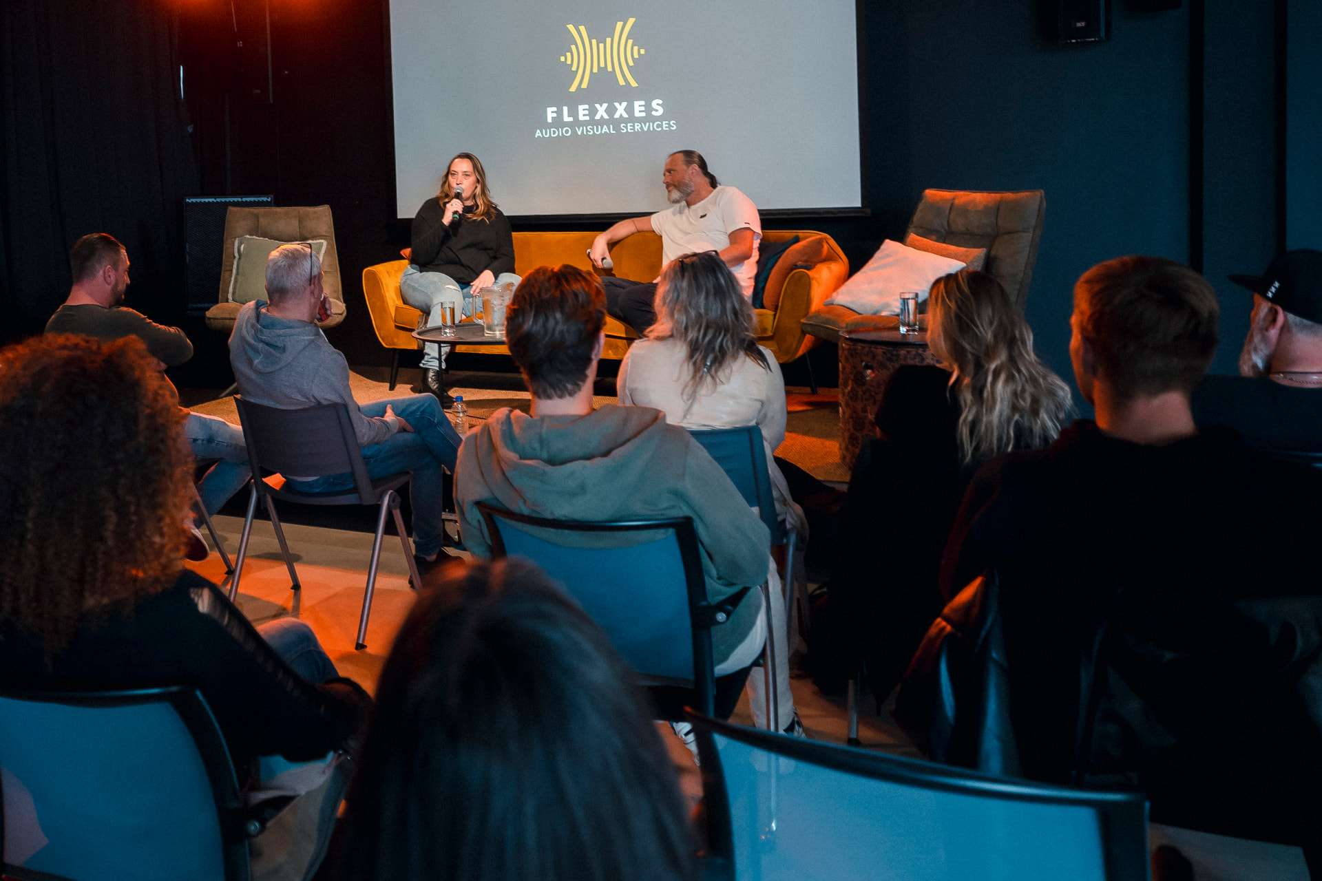 Panelists on the orange sofa seen from the audience during the 2023 edition