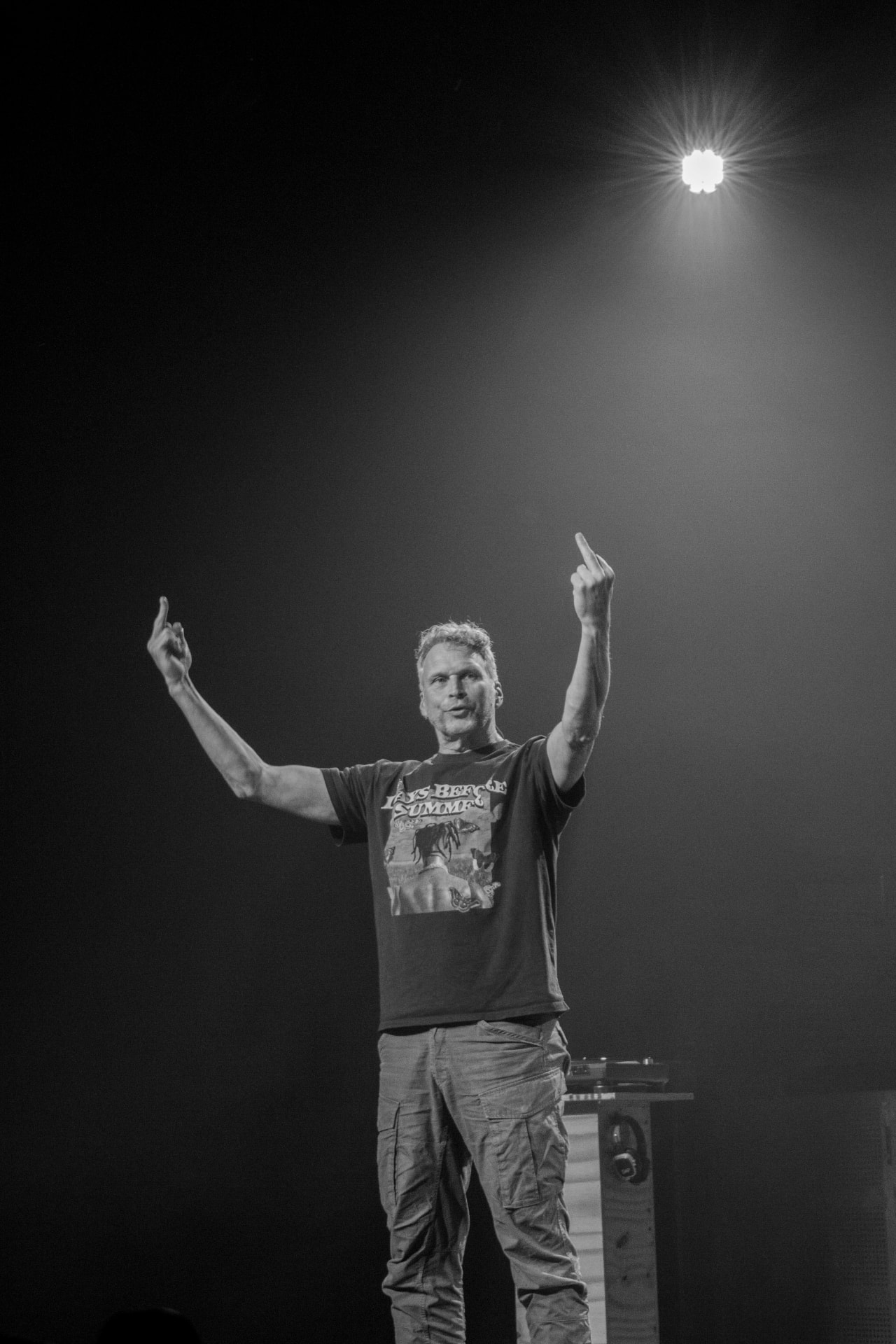 Performer with raised arms under a single spotlight during the theatre performance