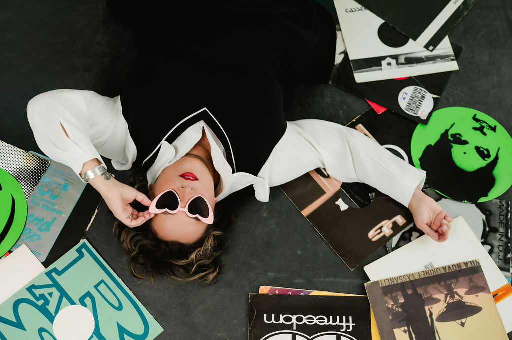 Michèle lying on the floor surrounded by vinyl records, lowering her heart-shaped sunglasses
