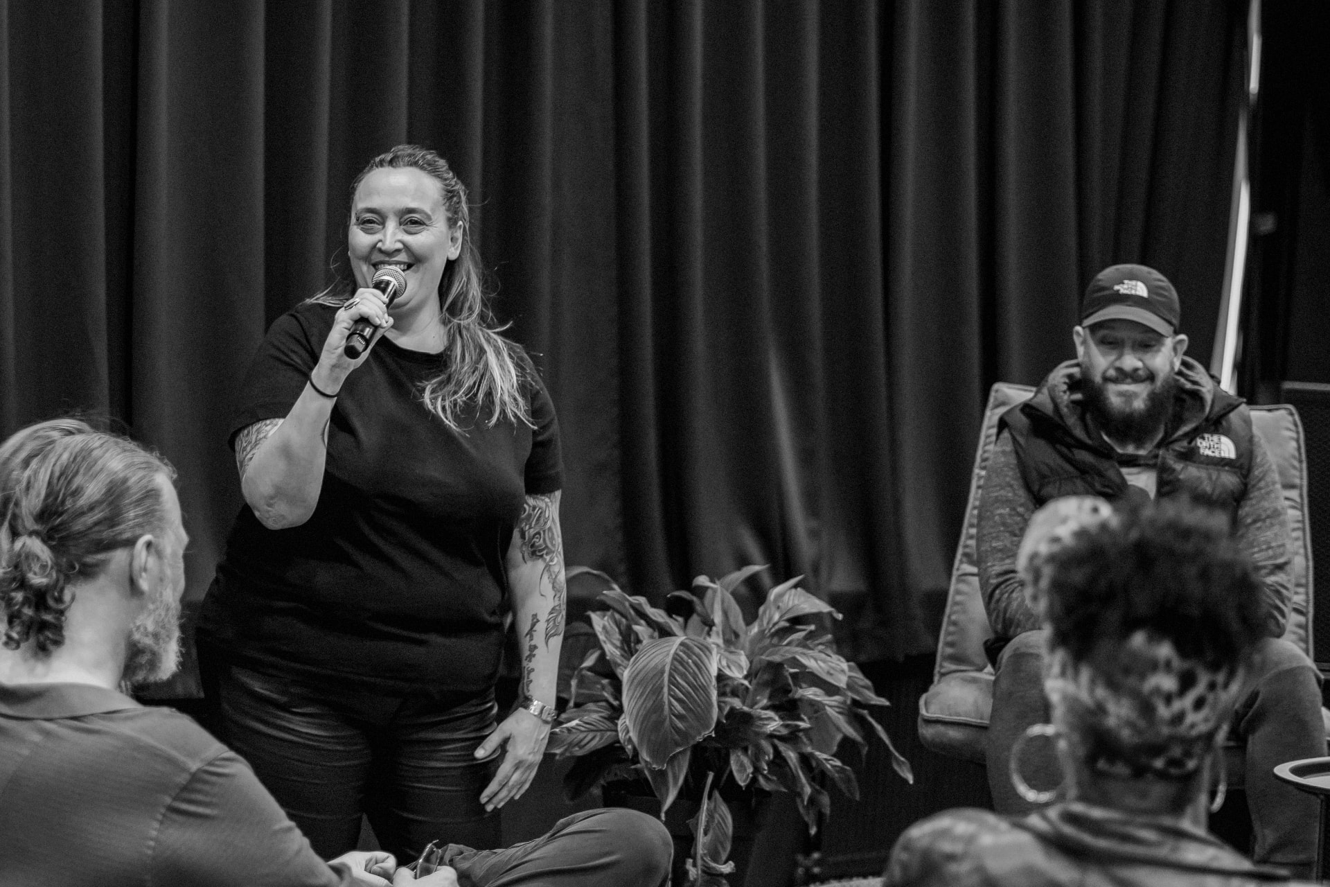 Moderator smiling with a microphone in front of the audience, 2023 edition