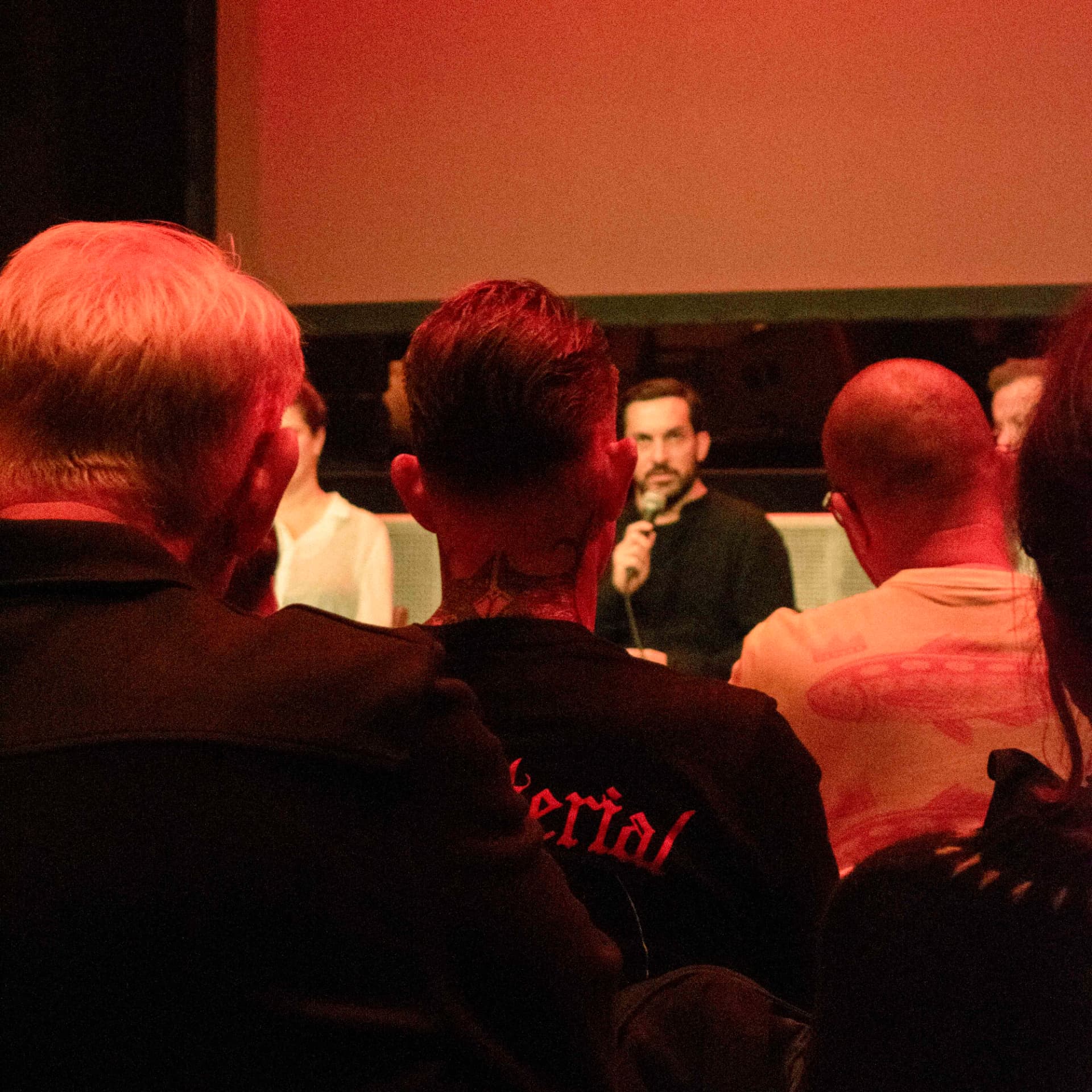 Speaker with a microphone addressing the seated audience in warm red light