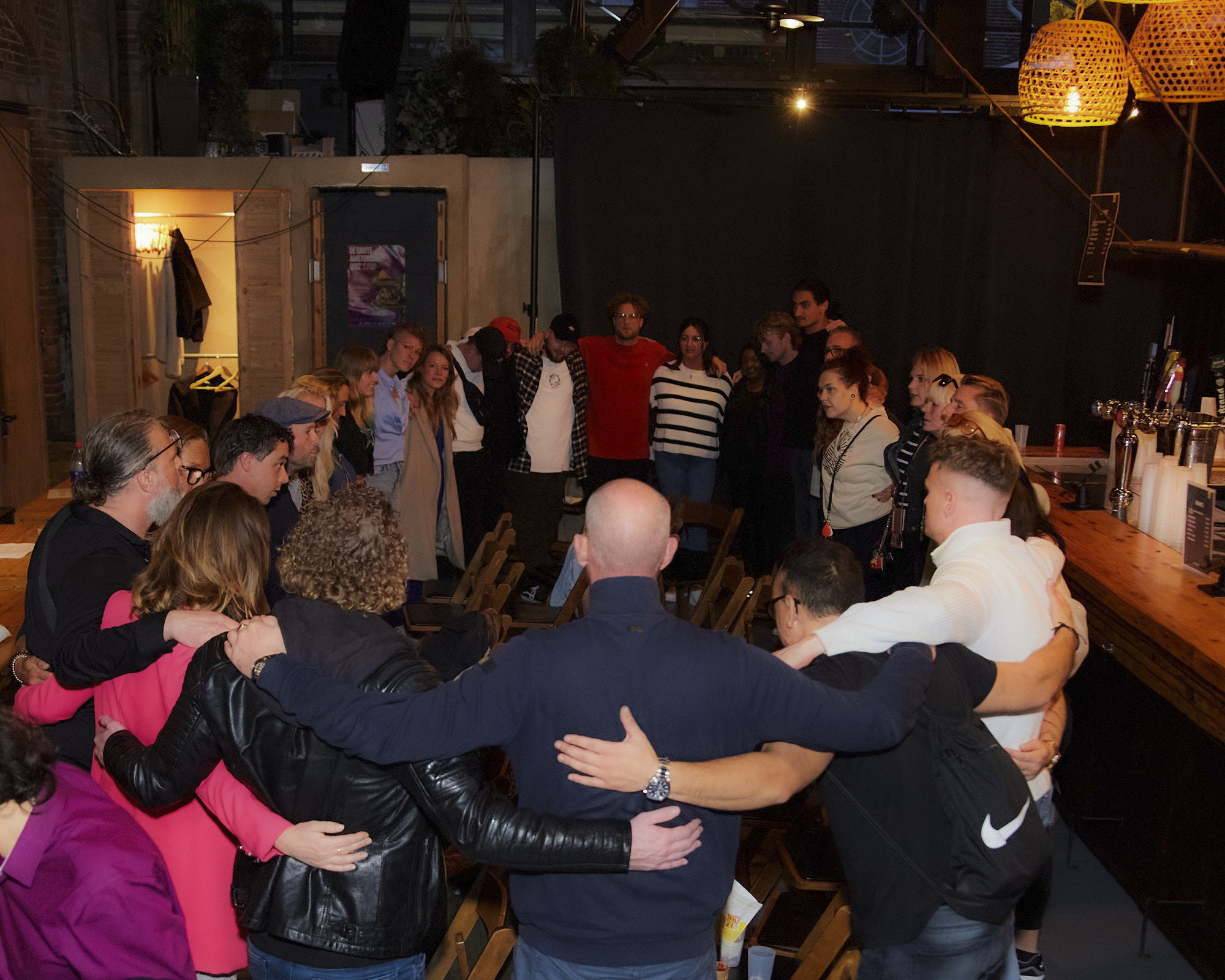 People standing in a circle with their arms around each other in a warm-lit room