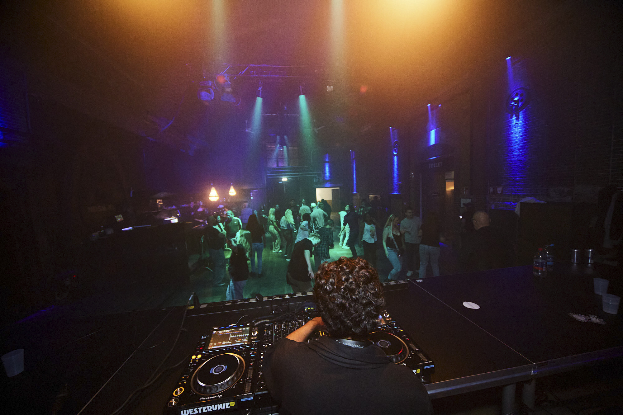 DJ performing over a busy UNWASTED dancefloor seen from behind the decks