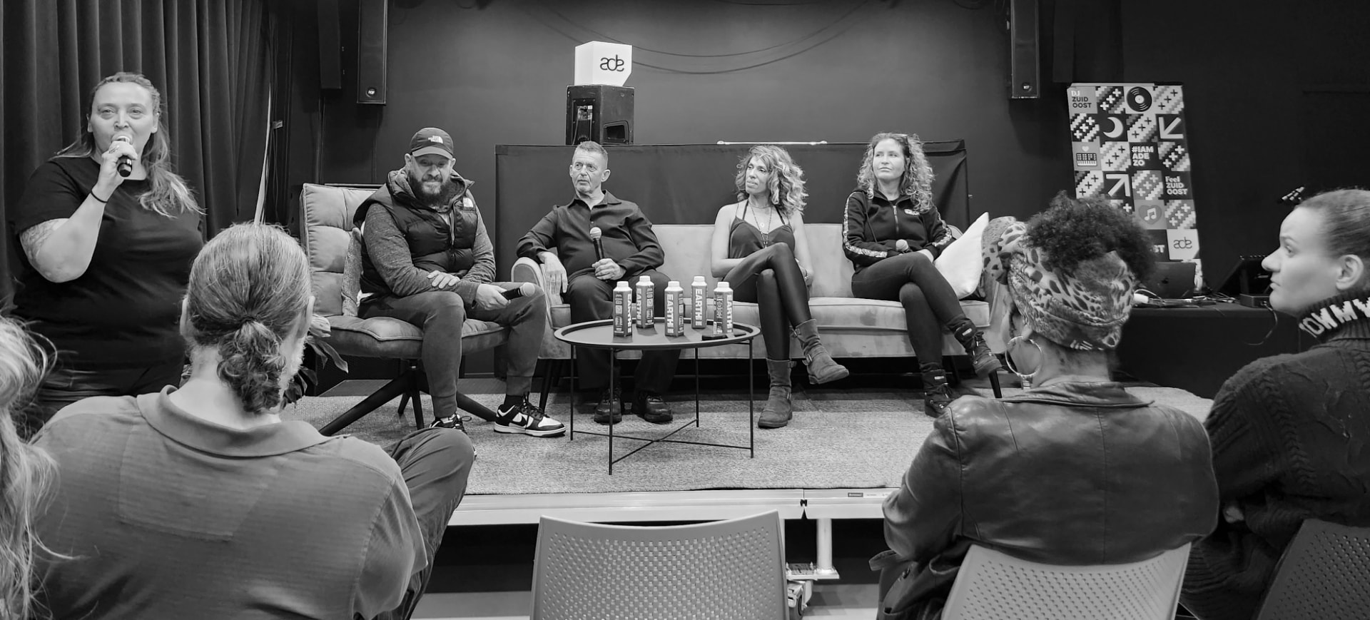 Wide stage view of the panel with a moderator and the audience, 2023 edition