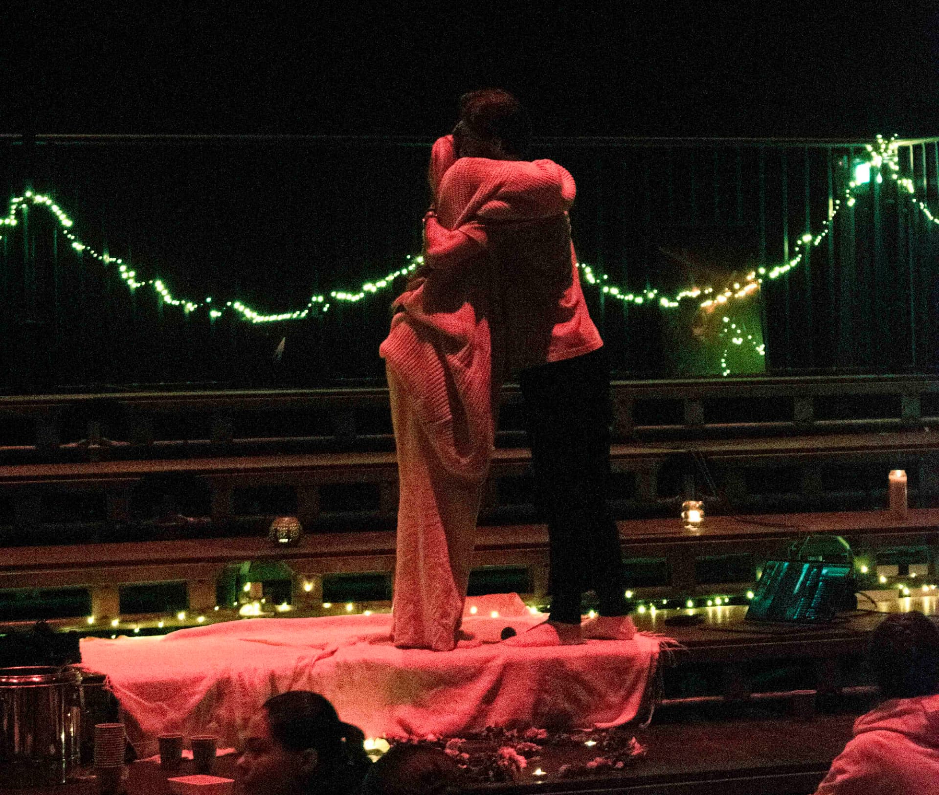 Two participants embracing in red light on a candlelit stage during the closing wellness moment