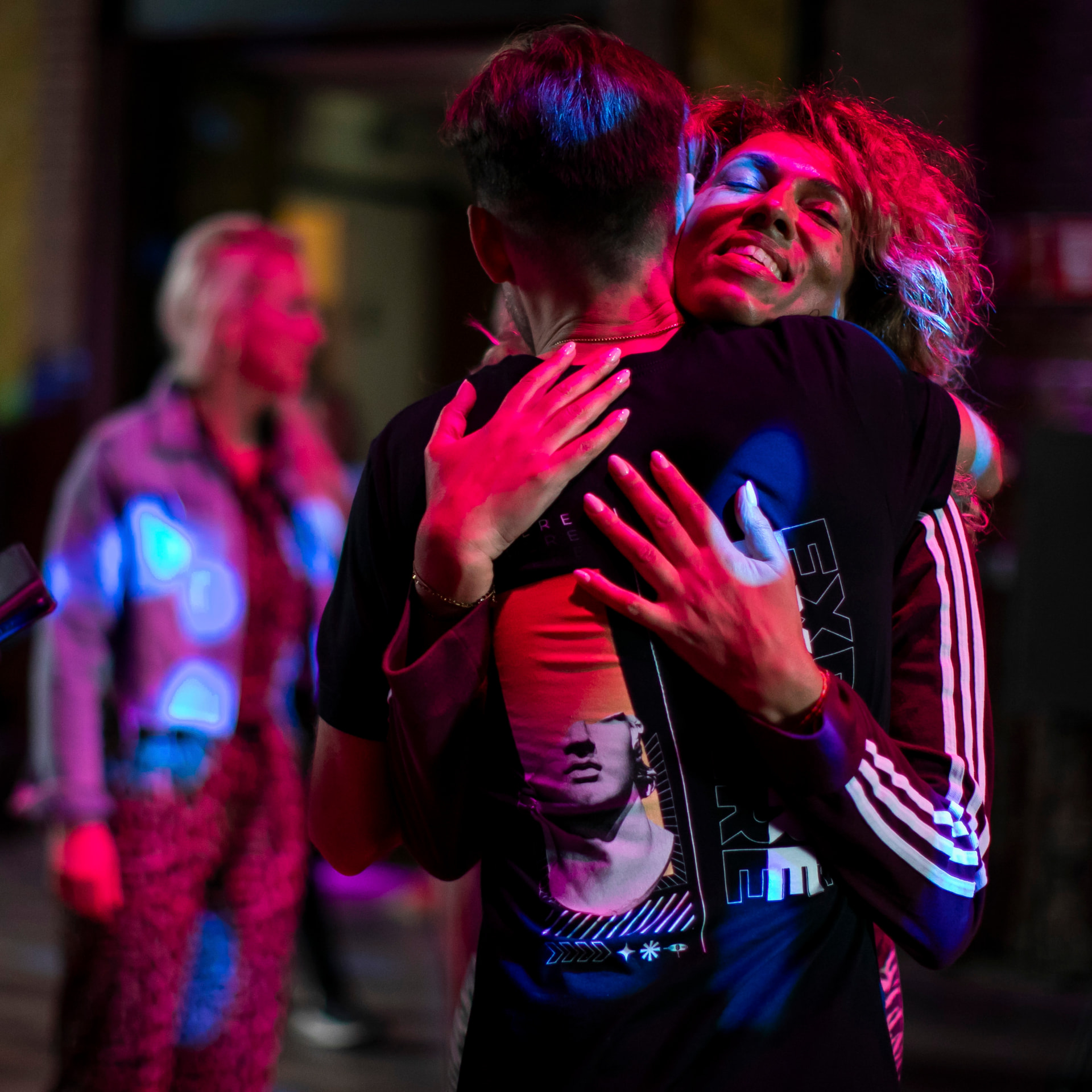 Two people embrace in red and blue club light, one smiling with eyes closed